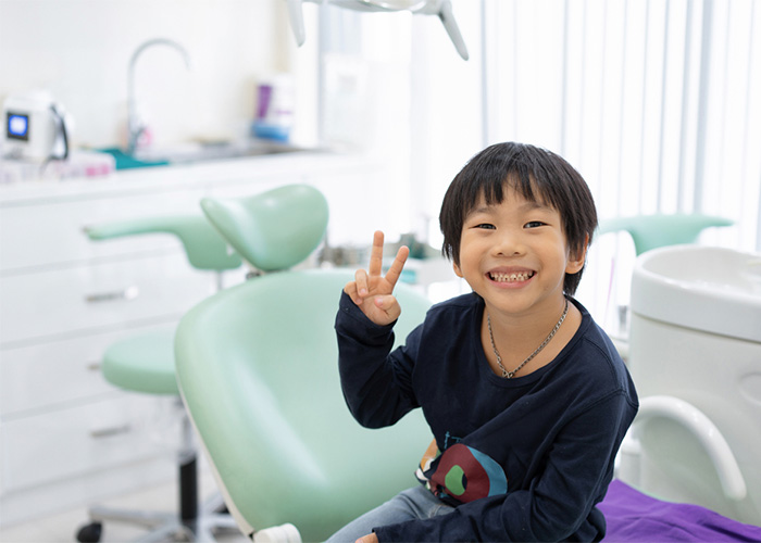 child sitting on the exam chair smiling and giving the peace sign