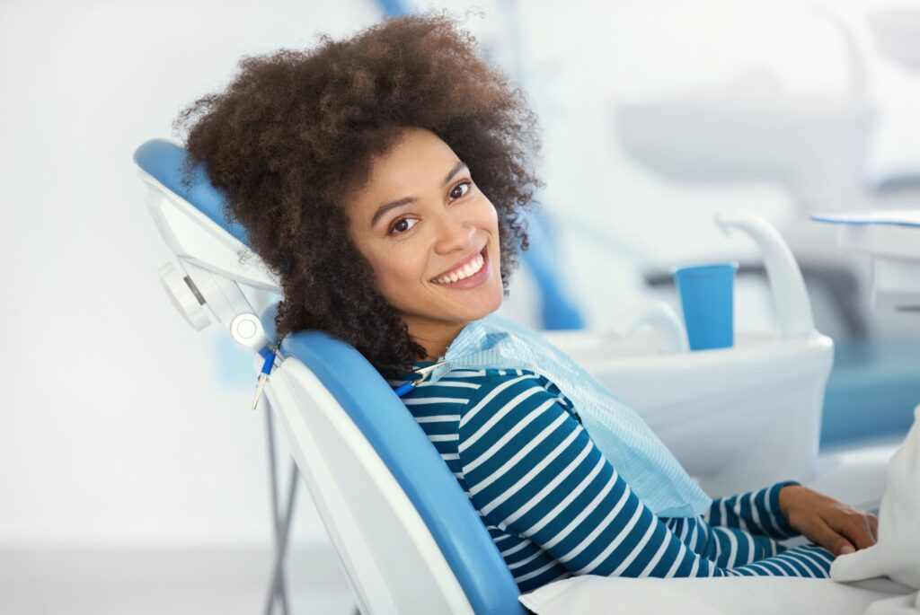 woman with black hair sitting in dental chair looking at camera and smiling